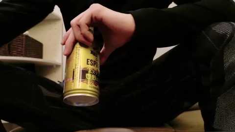 Media: A close-up video of a person with light skin tone, wearing black clothing, holding a yellow and black aerosol can labeled \"ESPRESSO.\" The background shows a beige wall and a wicker basket. The setting appears to be indoors.