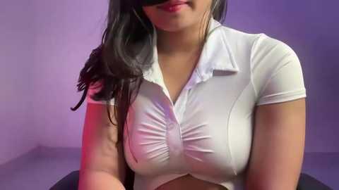 Media: Video of a young woman with medium brown skin and long black hair, wearing a tight, white, short-sleeved blouse that accentuates her medium-sized breasts, against a purple gradient background.