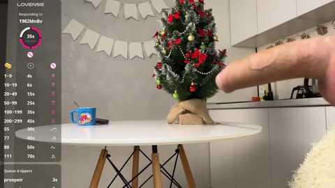 Media: A video of a modern kitchen with a white round table, decorated with a miniature Christmas tree and a blue mug. A hand is pouring milk into the mug.