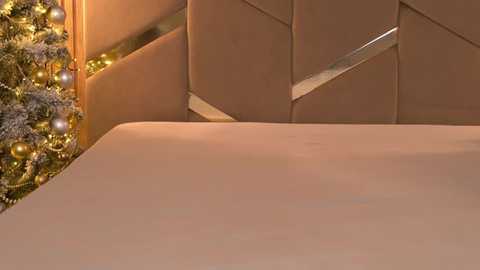 Media: A video showcasing a neatly made bed with a beige comforter. In the background, a festive Christmas tree adorned with gold and silver ornaments and a subtle snow effect is partially visible. The setting exudes warmth and holiday cheer.