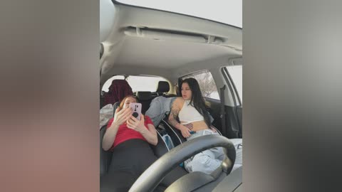 Media: A candid photo shows two women in a car, one in a red shirt, the other in a white crop top, both smiling and chatting.