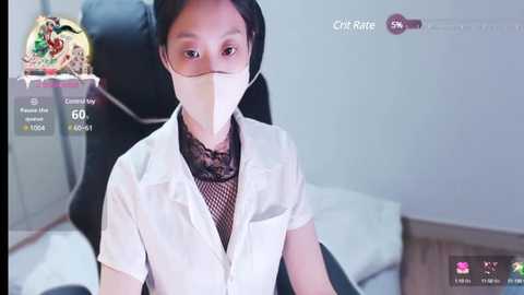 Media: Video of an East Asian woman in a white lab coat, face mask, and black lace blouse, sitting in a chair with a gray background.