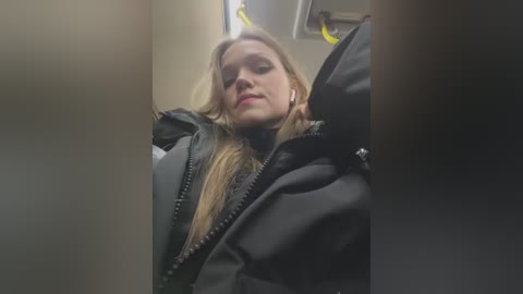 Media: Video of a blonde woman wearing a black coat, sitting in a bus, head tilted back, looking tired.