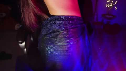 Media: A video of a woman with long, wavy brown hair, wearing a black sequined dress, illuminated by blue and red stage lighting, captured from the side.