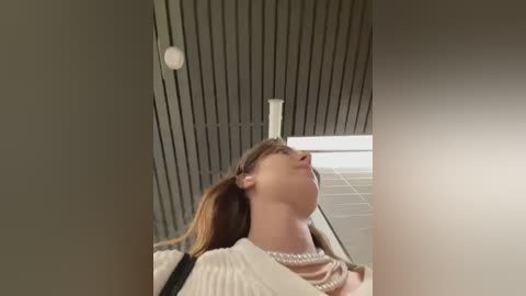 Media: A video captures a woman with brown hair and a white blouse, tilted back in a chair, appearing to be in a trance-like state. The background features a modern, angular ceiling and a window with blinds.