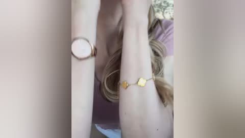 Media: Video of a fair-skinned woman lying on her side, wearing a pink top and gold bracelet, with blonde hair visible. A gold watch is on her left wrist.