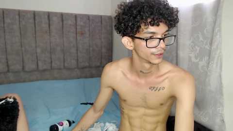 Media: Video of a shirtless, young, slender Asian man with curly hair and glasses, standing in a dimly lit bathroom with a light blue shower curtain and towels.