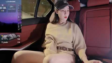 Media: A video of a young Asian woman in a beige sweater and cap, sitting in the back seat of a car at night, with a digital display showing location and time.