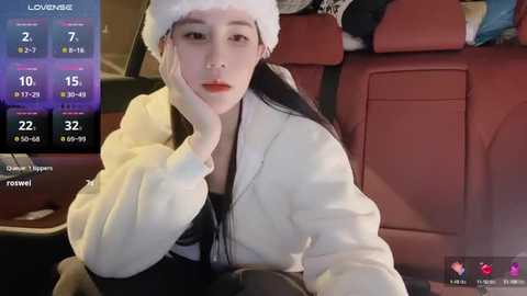 Media: A video of an East Asian woman with long black hair and fair skin, wearing a Santa hat and a white fluffy jacket, sitting in a red car, with a digital display showing weather details in the background.