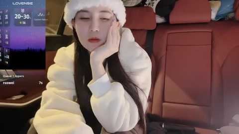 Media: A video of a young Asian woman with long black hair, wearing a Santa hat and white robe, sleeping in a car seat, surrounded by cluttered, dimly lit surroundings.