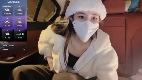 Media: Video of an Asian woman in a white robe and Santa hat, wearing a face mask, sitting in a car, with a COVID-19 tracker screen in the background.