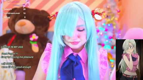 Media: A vibrant, colorful screenshot from a livestream featuring a light-skinned, anime-style girl with long blue hair, wearing a pink shirt and blue tie, with a plush teddy bear in the background.