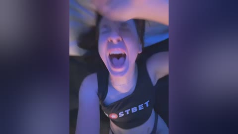 Media: A blurry, low-light video of a young woman with dark hair, wearing a black sports bra with the word \"STEBET\" in white, screaming with her mouth wide open, hands shielding her face.