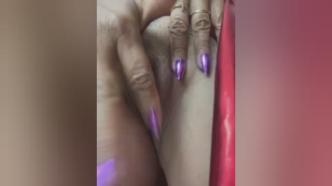 Media: Video of a close-up of a woman's hand with manicured, purple-painted nails gently touching her vulva, set against a gradient background of beige and pink.