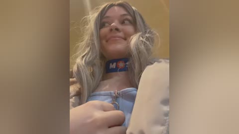 Video of a smiling, fair-skinned woman with long, wavy blonde hair, wearing a blue collar with \"M&M\" logo, a light blue top, and a leopard print jacket.