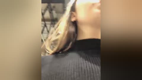 Media: Video of a woman with long, straight blonde hair, partially visible face, wearing a black ribbed top, in an indoor setting with blurred background.