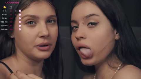 Media: Video of two young women with pale skin, dark hair, and similar facial features, wearing minimal makeup, with one sticking out her tongue, set against a dark background.