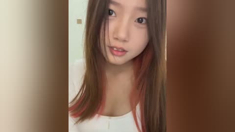 Media: Video of a young Asian woman with long, straight brown hair with red highlights, light skin, and small breasts, wearing a white top, standing in a doorway with blurred background.