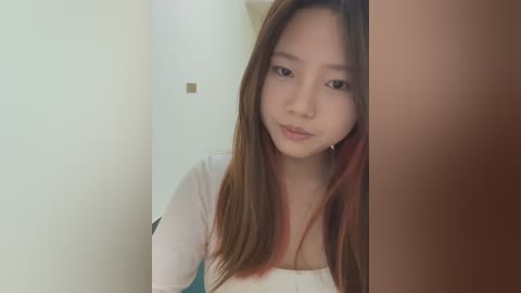 Media: Video of an East Asian woman with straight, shoulder-length brown hair and light skin, wearing a white top, partially obscured by a wooden door.