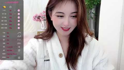 Media: Video of a smiling Asian woman with fair skin, long brown hair, and red lipstick, wearing a white bathrobe, in a well-lit, modern bathroom.