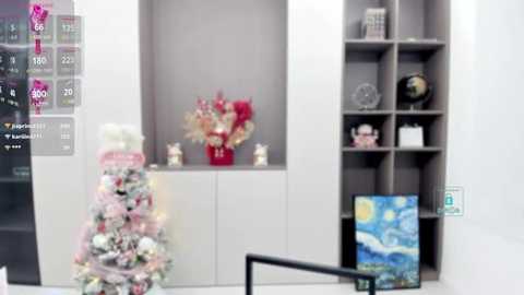 Media: Video of a modern living room with a Christmas tree adorned with white and pink ornaments, a white bookshelf holding decorative items, and a Monet painting on the wall.