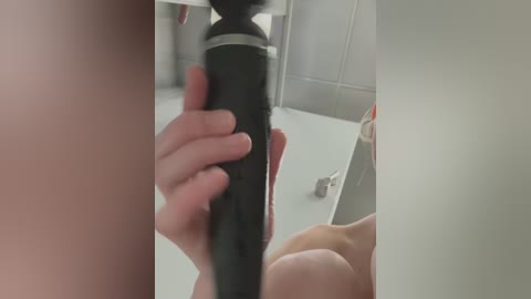 Media: A close-up video of a person holding a black hairdryer in a bathroom, with a blurred background showing a white sink and mirror.