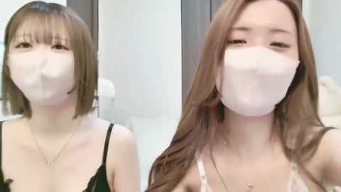 Media: Video of two young Asian women with short brown hair, wearing white face masks, black tank tops, and sitting in a modern bathroom with white tiles.