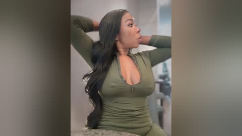 Media: Video of a dark-skinned woman with long black hair, wearing a low-cut olive green top, stretching in a bathroom with gray walls and a granite countertop.