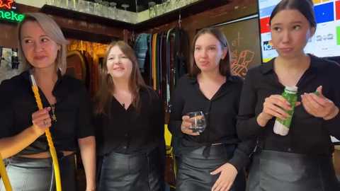 Media: Video of four women, two with blonde hair, two with brown hair, in black shirts and black skirts, holding drinks in a dimly lit bar, with a neon sign and hanging coats in the background.