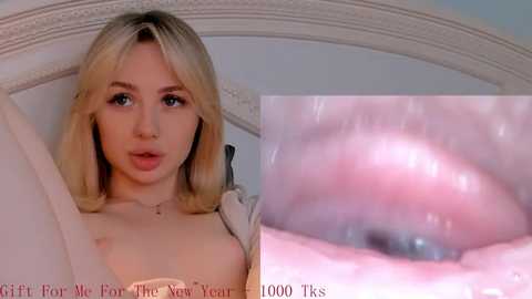 Media: Video of a young, blonde woman with fair skin and blue eyes, lying on a bed. The image shows her upper body, partially covered by a beige blanket. Text overlays indicate \"Gift For Members: $5.00 - New Year New Me - 1000 TSS.\