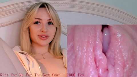 Media: Video of a smiling, blonde young woman with fair skin, wearing a white top, on a bed with an ornate headboard. Close-up of her vagina, showing pink, moist, and textured labia. Text overlays: \"Gift for Her - More Than New Year - 1000 Ties.\