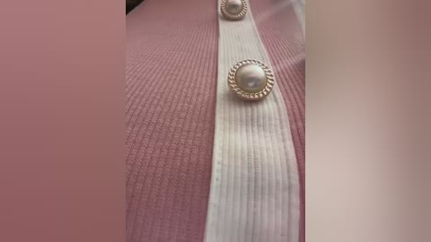 Video of a close-up view of a pink ribbed knit sweater with white ribbed cuffs and buttons, showing texture and details.