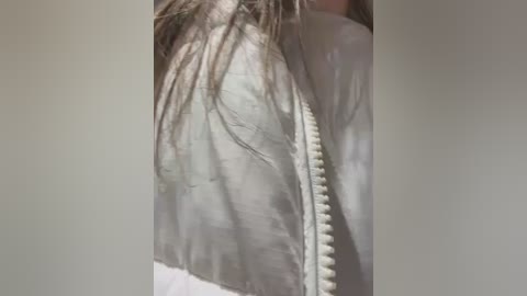 Media: A video of a person wearing a white jacket with a zip, their long brown hair partially obscuring their face, taken from a slightly low angle.