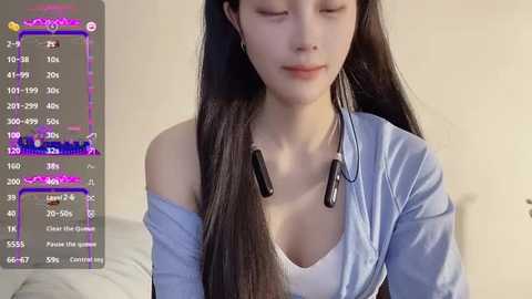 Media: Video of an Asian woman with long black hair, wearing a white tank top and off-shoulder blue shirt, with headphones on, in a softly lit room.