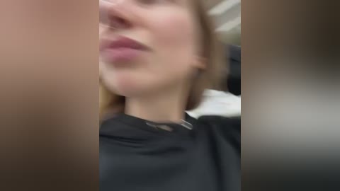 Media: A blurred video of a woman with fair skin and light brown hair, wearing a black turtleneck, seen from a side angle. The background is indistinct, possibly an indoor setting.