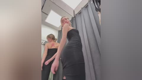 Media: A video of a blonde woman in a black dress standing in a fitting room, facing a mirror, revealing a red tattoo on her back.