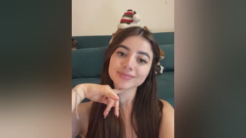 Media: A young woman with long brown hair and a white headband, smiling, sits on a teal couch, wearing a sleeveless top.