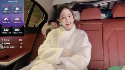 Media: A video of a smiling young woman with pale skin and dark hair, wearing a white fur coat, seated in a red car, with social media icons on the left.