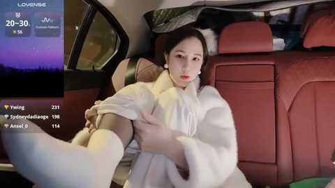 Media: Video of a woman in a white fur coat, sitting in a red leather car seat at night, wearing makeup.