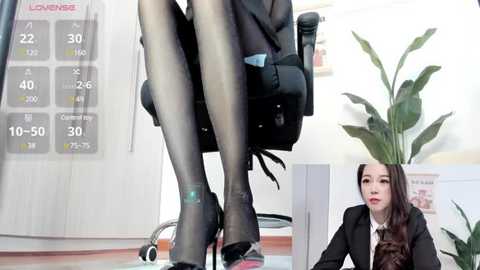 Media: Video of an Asian woman in a black business suit and heels, sitting on a black chair in an office with a calendar and potted plant.