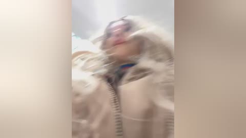 Blurry video of a person in a white fur-trimmed jacket, possibly a parka, with a red collar, captured from a low angle, with a fuzzy background.