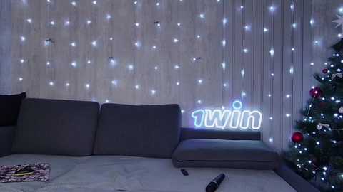 Media: Video of a cozy living room with a gray sofa, Thai script neon sign, fairy lights on wooden wall, and a decorated Christmas tree in the corner.