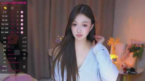 Media: A video of a young Asian woman with long black hair, wearing a light blue shirt, taken in a dimly lit room with a streaming interface overlay.