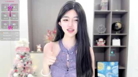 Media: A video of an East Asian woman with long black hair, wearing a purple Chinese-style dress, giving a thumbs-up in a modern, well-lit living room with a white wall and bookshelves.