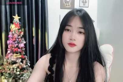 Media: Video of an East Asian woman with long black hair, wearing red lipstick, sitting in a chair, with a Christmas tree and star ornament in the background.