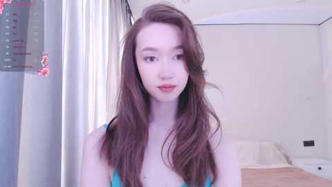 Media: A video of a young, fair-skinned woman with long, straight brown hair, wearing a turquoise bra, in a modern, brightly lit bedroom with white walls and minimalistic decor.