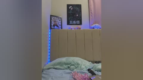 Media: Video of a messy bedroom with beige headboard, colorful pillows, a stuffed animal, a poster, and a bed with rumpled sheets, illuminated by blue LED lights.