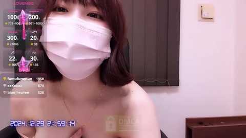 Media: A video of a young Asian woman with shoulder-length brown hair, wearing a white face mask and black top, captured indoors with a thermometer overlay.