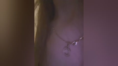 Media: A close-up video of a partially blurred woman's chest, with a silver necklace featuring a heart-shaped pendant, in a dimly lit room.