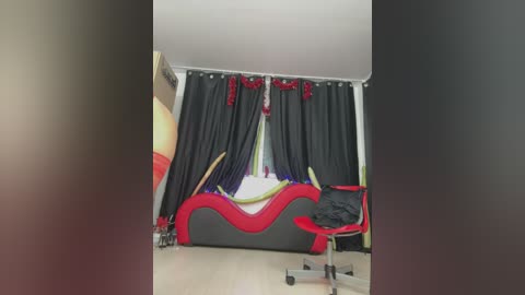 Media: Video of a modern, colorful bedroom with a black and red wavy headboard, black curtains with red bows, and a red chair with a black cushion, against a beige wall.